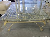 Front angled view showing glass top and cream painted metal base with scrollwork and gold accents.