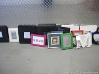 Black and white frames arranged on ground leaning against metal diamond plate wall, showing variety of sizes and some framed artwork with owl and panda prints and white wooden letters.