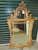 Full front view of gold-painted ornate mirror leaning against metal door