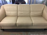Front view of cream leather sofa showing three seat cushions and smooth leather surface with minor stains.