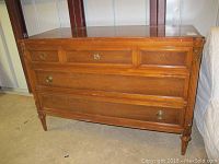 Front and angled views of a wooden dresser with three large drawers and brass-colored ring and round pull hardware. Shows scratches, chips, and missing hardware.
