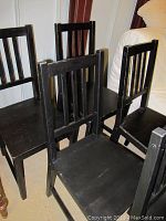 Set of six black wooden Ikea chairs arranged in a room showing side and angled views, highlighting chair design and scratches on surfaces.