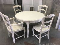 Overview photo showing the round white distressed table surrounded by four matching chairs, two with armrests and two without.