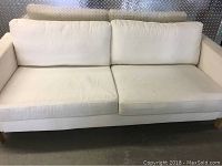 Front view of white IKEA sofa showing two seat cushions and two back cushions, fabric stained and worn.