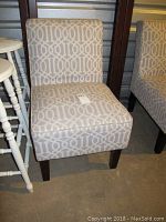 Front angled view of upholstered chair with gray geometric patterned fabric and dark wood legs.