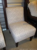 Photo of upholstered accent chair with light gray geometric patterned fabric and dark wood legs with wear.