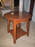 Brown wooden round end table with visible scratches on top and chips on legs, standing on carpeted floor.