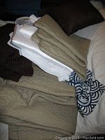 Stack of beige and white quilted curtain panels, large patterned blue and white pillow cover, and brown knitted pillow covers.