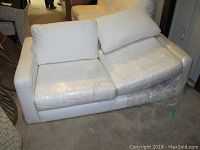 Front angle of off white IKEA loveseat showing two seat cushions and two back cushions wrapped in clear plastic. Some visible staining on fabric.