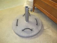 Top and angled view showing the round concrete base, central metal pole with knob, and four bent metal handles.