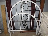White metal headboard and footboard leaning against a wall, showing the design and paint condition with visible scratches.