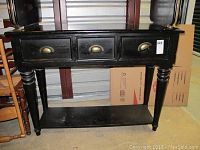 Front view of black wooden entry table showing three drawers with brass cup handles and bottom shelf.