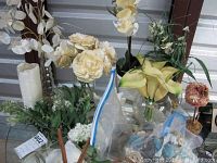 Overall view showing several vases with artificial flower arrangements, white pillar candle, and some decorative baskets and floral foam pieces