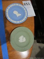 Two Wedgwood jasperware small plates, blue and green, showing classical white relief designs and decorative borders.