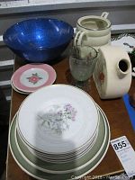 Lot photo showing large blue glass bowl, collection of floral plates, clear glass, and two floral pitchers.