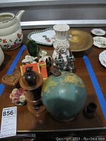 Photo of assorted decorative items on wooden surface including globe, figurines, vase, bowl, and plates