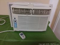 Full view of Frigidaire window air conditioner unit installed with window mounting kit and front vents visible, placed on green surface.