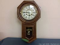 Regulator wall clock in wooden frame with glass front showing clock face and pendulum chamber