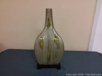 Front view of the tall pottery vase on its base, showing the elongated body with gray and yellow glaze accents