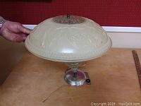 Full view of vintage ceiling light fixture showing frosted glass bowl with embossed leaves and floral design, metal base, and central clear glass element.