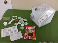 Full view of pasta maker with discs, plastic accessories, and manuals laid out on green surface
