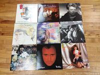Nine assorted LP vinyl records arranged on floor, featuring artists including Beach Boys, ABBA, Phil Collins, A-ha, Air Supply, and Lionel Richie.