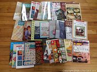 Photo of full collection of 27 quilting books arranged on wooden floor, showing colorful covers and various quilting topics.