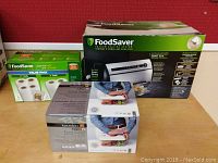Photo showing the boxed FoodSaver vacuum sealing system, value pack rolls, and vacuum seal containers boxed set.