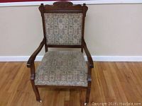 Front view of the antique wooden chair showing upholstery and carved top rail.