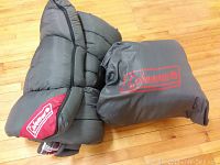 Two gray Coleman sleeping bags; one rolled up and the other packed in a gray Coleman storage bag