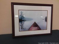 Framed print showing a red canoe on a calm lake with trees and mist in the background on a beige wall.