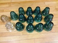 Fifteen Hemingray glass insulators arranged on wooden floor, mostly dark green with two clear ones.