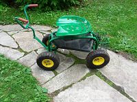 Side view of the green garden caddy showing the large four wheels, seat, and handle with grips.