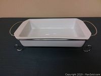 Top side view of the white ceramic rectangular casserole dish resting on its silver metal stand showing handles and dish shape.