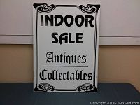 Front view of the sale sign displaying the text "INDOOR SALE Antiques Collectables" with decorative corners in black on white.