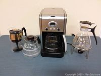 Cuisinart coffee maker with three glass carafes placed on table, showing overall lot contents