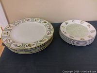 Two stacks of decorative botanical pattern plates, one stack with wider rims and colorful plant motifs, the other stack with narrower rims and green floral design.