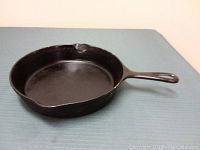 Cast iron fry pan shown from side and handle view on blue surface