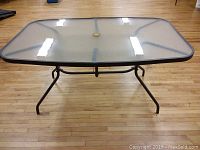 Top view of patio table showing clear tempered glass surface with slight reflections and central hole for umbrella insertion.