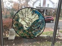 Photo of the round peacock stained glass panel hanging in front of a window