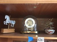 Shelf with white carousel horse music box on wood base, Kundo brass dome clock, and Asian miniature tree in ceramic bowl
