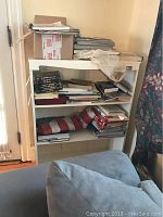 White painted wooden bookshelf filled with assorted papers, books, and boxes, taken from the left front angle.