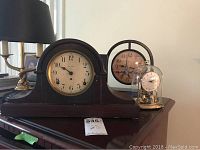Photo showing all three clocks together on a dresser: the large dark wood Seth Thomas mantle clock, the medium brassish Schatz clock with plastic cover, and the smallest battery-operated metal clock with dome