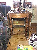 Front view of the wooden bar or tea cart showing drawer, two shelves, spindle legs, and two wooden wagon wheels on sides.