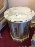Photo showing round marble top table with decorative cream and gold base and metal handles on door.