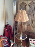 Floor lamp with beige pleated lampshade, brass base, and built-in round glass table