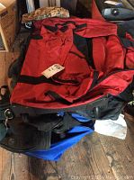 Red and black travel bag on top of other bags, showing handles and large storage area