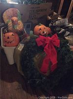 Photo of assorted holiday decorations including two ceramic pumpkin containers and a Christmas wreath with large red bow.