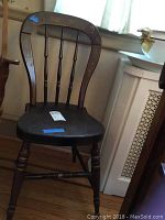 Side profile and seat of a vintage wooden chair with spindle back and wear marks.