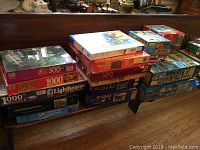 Various stacks of boxed jigsaw puzzles showing different brands and themes with piece counts from 300 to 1000 pieces.